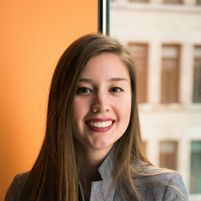 Smiling woman with long brown hair in a gray blazer